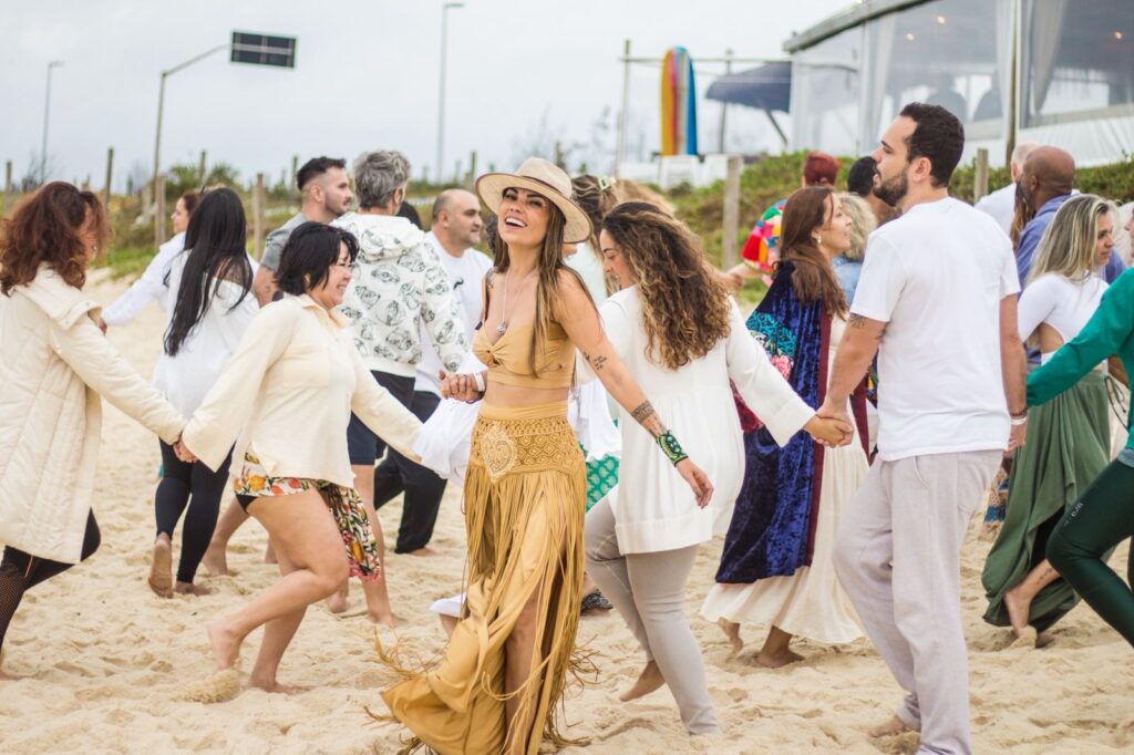Grupo de pessoas reunidas na Praia da Reserva, Rio de Janeiro, de frente para o mar, durante o ritual de cacau Conexões Cacau ao nascer do sol.